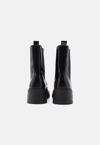 Μαύρα μποτάκια μέχρι τον αστράγαλο με γυαλιστερή επιφάνεια, που διαθέτουν ελαστικές πλαϊνές πάνες και ανθεκτικούς τετράγωνους τακουνί τ. Λείες υφές και θηλιές στην πλάτη.