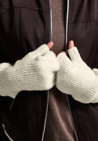 Fingerløse handsker lavet af blødt, struktureret, lys grå stof med ribbet design. Båret af hænder, der er placeret sammen, en del af en mørk jakke er synlig.