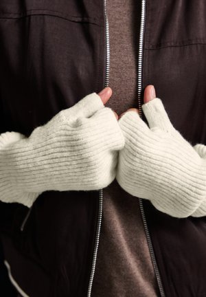 Gants sans doigts en tissu doux, texturé et gris clair, avec un motif à côtes. Portés par des mains positionnées ensemble, une partie d'une veste noire est visible.