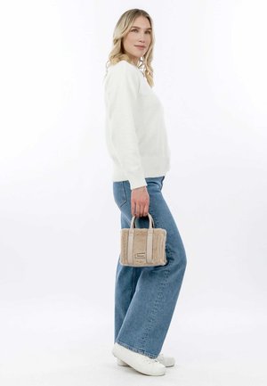 Pull léger en crème ; jeans bleus évasés ; petit sac à main beige à texture en fourrure et design structuré, tenu à la main. Fond blanc.