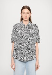 Short-sleeve button-up shirt in lightweight fabric, featuring a black and white spotted pattern, and a straight hem with front pockets.