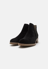 Bottes cheville en daim noir avec un bout arrondi et des panneaux latéraux élastiques. Dotées d'un talon bas empilé et d'une semelle en caoutchouc beige.