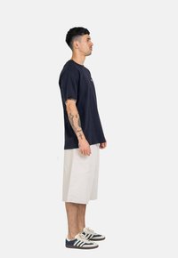 Navy cotton t-shirt with short sleeves and a round neckline, paired with knee-length beige shorts and navy sneakers featuring white stripes.