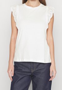White cotton top featuring short sleeves with broderie anglaise detailing. Straight-cut design with a crew neckline. Paired with dark jeans.