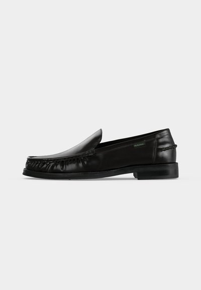 Mocassin en cuir noir à enfiler avec des détails tressés sur les côtés et un petit talon sur fond blanc uni.