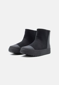 Czarne botki za kostkę z teksturowaną gumową podeszwą, gładkim materiałem cholewki i wzmocnionym czubkiem. Prosty, nowoczesny design bez widocznych zapięć.
