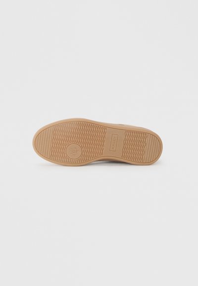 Semelle de chaussure en caoutchouc beige avec une surface texturée, arborant un logo circulaire et une semelle à motif pour une meilleure adhérence. Design minimaliste sans accents visibles.