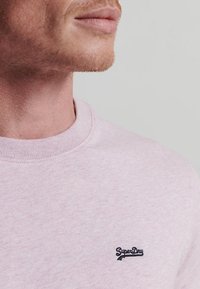 Lichtroze sweatshirt van textuurstof, met een ronde hals en een klein marineblauw 'SuperDry' logo op de linker borst.
