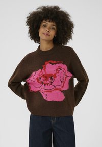 Brown knitted sweater featuring a large, vibrant pink floral design. The fabric appears soft, with ribbed cuffs and a round neckline.
