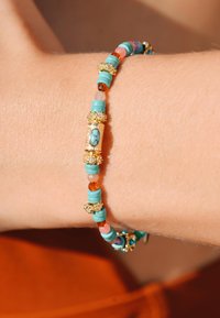 Bracelet en turquoise et perles multicolores avec des accents dorés, présentant diverses textures et motifs, porté sur un poignet.