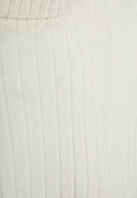 Close-up van crèmekleurige ribgebreide stof met verticale textuurstripes en een afgeronde halslijn.