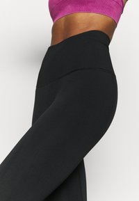 Černé legíny s vysokým pasem vyrobené z elastického materiálu, které mají hladkou texturu a přiléhavý střih pro pohodlí a pohyblivost.