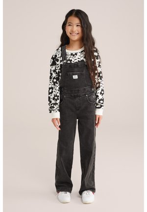 Salopetă din denim negru cu picioare largi, buzunare frontale, bretele ajustabile și o cămașă albă cu mâneci lungi care prezintă un model floral îndrăzneț.