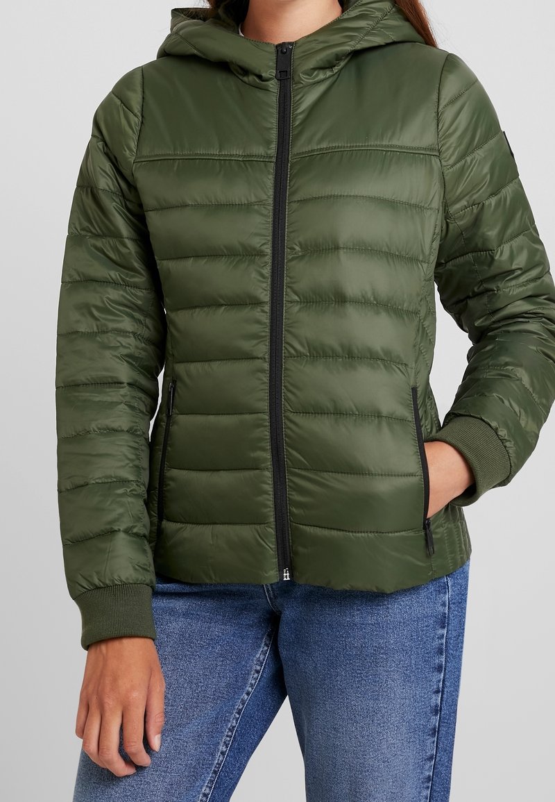 Grüne gestepfte Pufferjacke mit Kapuze, ausgestattet mit einem Reißverschluss vorne und gerippten Bündchen. Glatte Textur mit seitlichen Taschen.