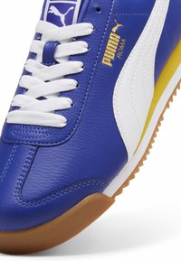 PUMA Roma-sneakers i blått läder, med vita detaljer, guldlogotyp och en texturerad gummisula. Klassisk snördesign.