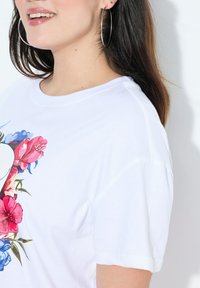 Camiseta de algodón blanca con un diseño floral en rosa, rojo y azul, con mangas cortas y cuello redondo. Gran gráfico en la parte delantera.