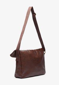 Brown leather messenger bag with a soft texture, adjustable two-tone strap, and minimalistic design. Sturdy stitching and subtle hardware accents.