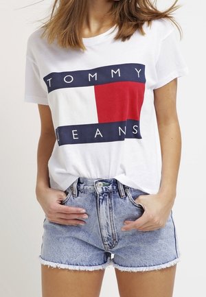 Donna che indossa una t-shirt bianca con il logo Tommy Jeans infilata in shorts di jeans azzurri a vita alta con orli sfrangiati.