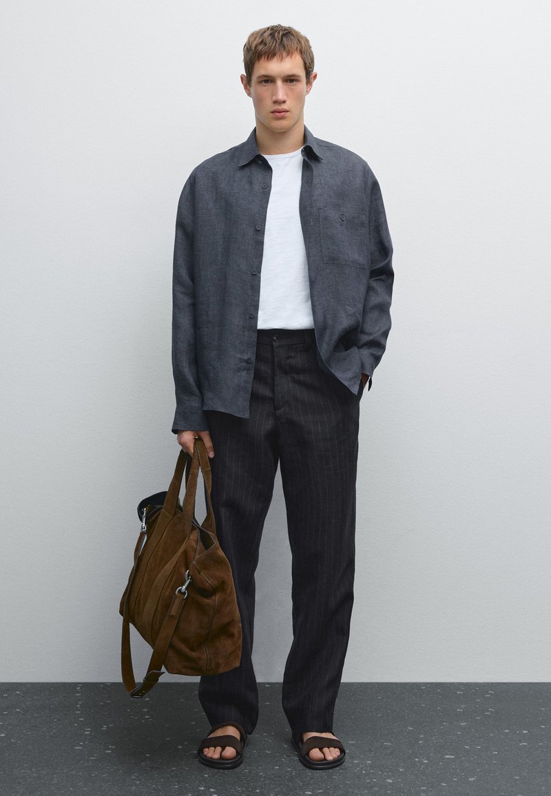 Dark gray linen shirt, white T-shirt, pinstriped dark trousers, brown suede bag, black sandals. Simple design, minimal detailing.