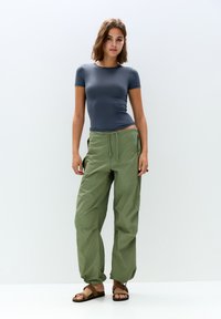 Lahka, prilega tma siva majica s kratkimi rokavi v kombinaciji s širokimi olivno zelenimi cargo hlačami in rjavimi sandali. Vidne teksture blaga.