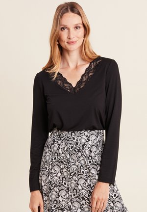 Haut à manches longues noir avec un décolleté en V bordé de dentelle, associé à une jupe noir et blanc à motifs avec des designs floraux.