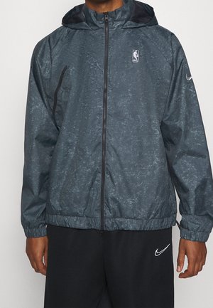 Dunkelgraue Kapuzenjacke mit Reißverschluss, subtil gemustert, NBA-Logo auf der Brust, und schwarze Hose mit weißem Nike-Swoosh-Logo.
