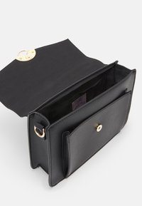 Borsa a tracolla in pelle nera con una chiusura dorata, caratterizzata da un design aperto, una tasca esterna e un'etichetta interna. Finitura testurizzata, hardware minimale.