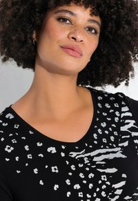 T-shirt nera con scollo a V, caratterizzata da una stampa animalier argentata. Tessuto morbido con una superficie liscia, ideale per l'uso quotidiano.