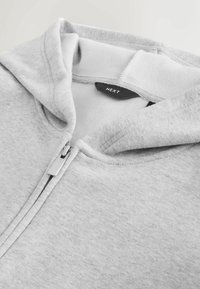 Szara bluza z kapturem na zamek z miękkim polarem wewnątrz, spiczastym kapturem i metalowym uchwytem zamka. Etykieta nosi napis "NEXT."