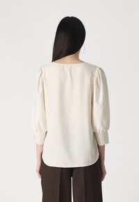 Blusa crema con maniche a sbuffo e bordo in pizzo sui polsini. Tessuto morbido con scollatura rotonda. Vestibilità casual e rilassata.