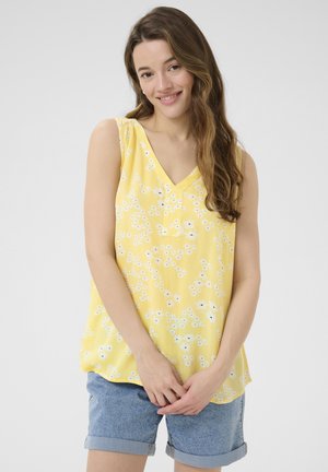 Haut sans manches jaune avec un motif floral blanc, décolleté en V et texture légère. Associe avec un short en denim délavé.