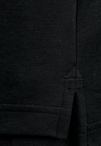 Schwarzer Baumwollstoff mit einem Nahtdetail in Form eines dreieckigen Stiches. Glatte Textur mit leichtem Glanz und einem seitlichen Schlitz für das Design.