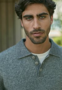Suéter gris con canalé, cuello con solapa y tapeta de tres botones, llevado sobre una camisa blanca. Textura suave, diseño casual.