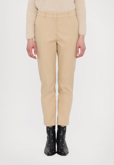 Pantalons beiges ajustés avec une coupe droite, taille mi-haute et deux poches latérales. Portés avec des bottines noires à couper le souffle avec des accents en métal argenté.