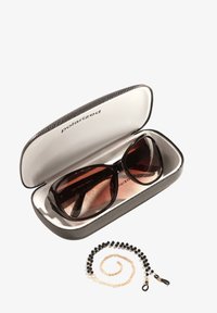 Polaryzacyjne okulary przeciwsłoneczne w szarym, teksturowanym etui. Okulary mają ciemnobrązowe soczewki oraz odważny, oversize'owy design. W zestawie z czarnym i złotym koralikowym łańcuszkiem.