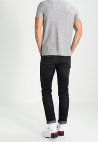 Grå kortærmet t-shirt, sorte slim-fit jeans, hvide sneakers med røde accenter. Synlig syning og opslåede manchetter på jeans.