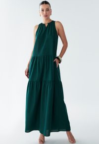 Robes maxi vert à volants avec un col bijou et un détail en trou de serrure. Tissu lisse, sans manches, poches latérales et silhouette décontractée.