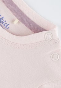 Light pink short-sleeve shirt with a soft texture, featuring a lavender neckline and snap closures at the shoulder for easy dressing.