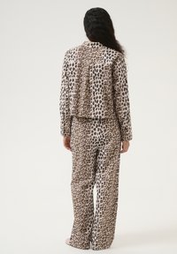 Luipaardprint pyjama set in beige en bruin tonen; losse top met lange mouwen en bijpassende rechte broek. Zachte, gestructureerde stof.