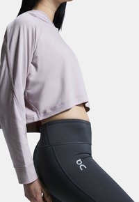 Zkrácená světle růžová mikina s dlouhými rukávy a plochými švy, kterou doplňují černé legíny s vysokým pasem s logem na stehně.