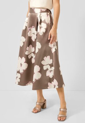 Woman wearing brown midi skirt with large white and pink floral print, paired with beige heeled sandals and a cream top.