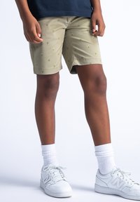 Pantaloni corti khaki con piccoli motivi di palme verdi, in tessuto leggero, e tasche laterali. Abbinati a sneakers bianche e calze bianche a rete.