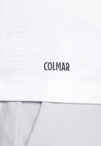 Chemise de sport blanche avec un motif texturé, arborant un logo "COLMAR" noir brodé à l'ourlet. Tissu léger, texture lisse.