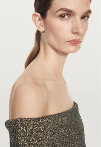 Schulterfreies Oberteil aus metallisch grünem Strickstoff, mit figurbetonendem Schnitt und strukturierter Oberfläche, das Schlüsselbein und Hals betont.