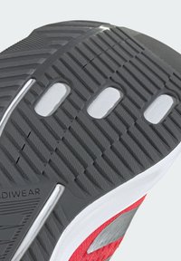 Shoe sole featuring a textured gray rubber material with deep grooves, white accents, and cut-out sections for improved grip and flexibility.