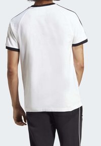 Pánské bílé sportovní tričko s černým lemem. Má krátké rukávy a volný střih. Tkanina vypadá hladce a design má raglánové rukávy.