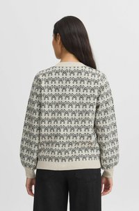 Pull léger beige clair avec motif de nœuds noirs, ourlet et poignets côtelés, col rond et manches bouffantes ; texture douce et coupe ample.