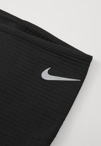 Tissu athlétique noir avec un motif texturé, présentant un logo Nike argenté sur le côté et un ourlet plat et cousu pour un maintien sécurisé.