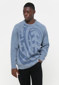 Maglione lavorato a maglia azzurro chiaro con un motivo testurizzato e polsini a coste. Presenta un audace design del logo in blu scuro sul fronte.