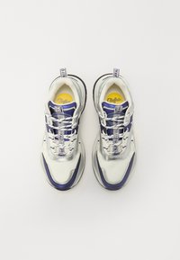 Hvite og marineblå sneakers med et teksturert mesh-overdel, lagdelt design, reflekterende detaljer og en gul logo på innersålen. Har snøring.